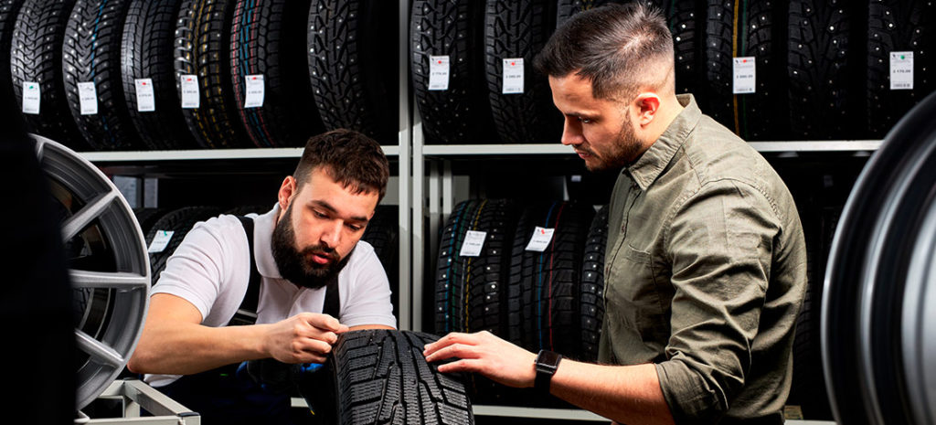 Mecánico junto a cliente examinando las dimensiones de un neumático