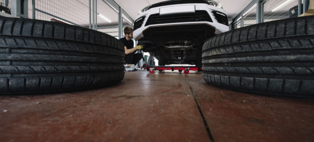 Dos ruedas de coche delante de un vehículo blanco que está siendo reparado por un mecánico