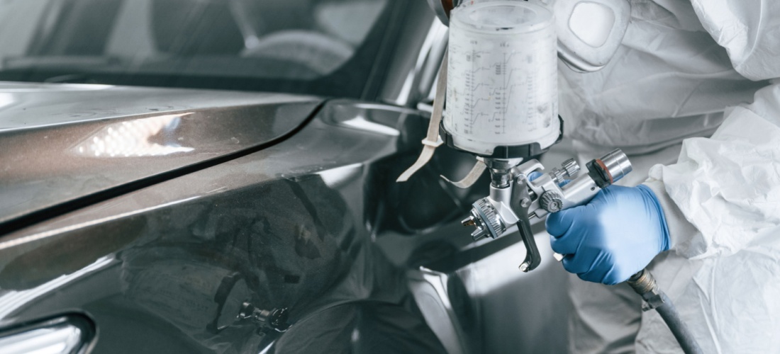 Operario, vestido con protección EPI, sostiene una pistola de pintura para coches en una manos.