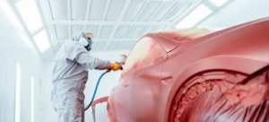 Un hombre con mono de trabajo blanco y mascarilla pinta un coche en rojo