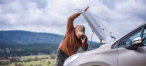 Hombre con gorra tirado en la carretera abre el capó del coche para revisar porque el vehículo no arranca