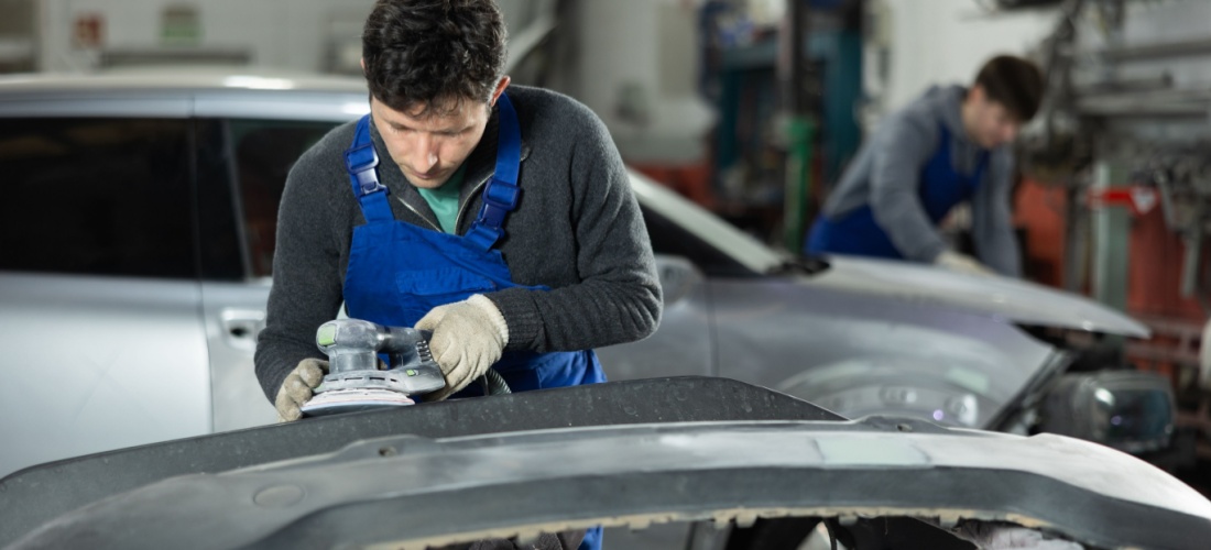 Mecánico pasa una lijadora a un paragoples de un coche en un taller mecánico.