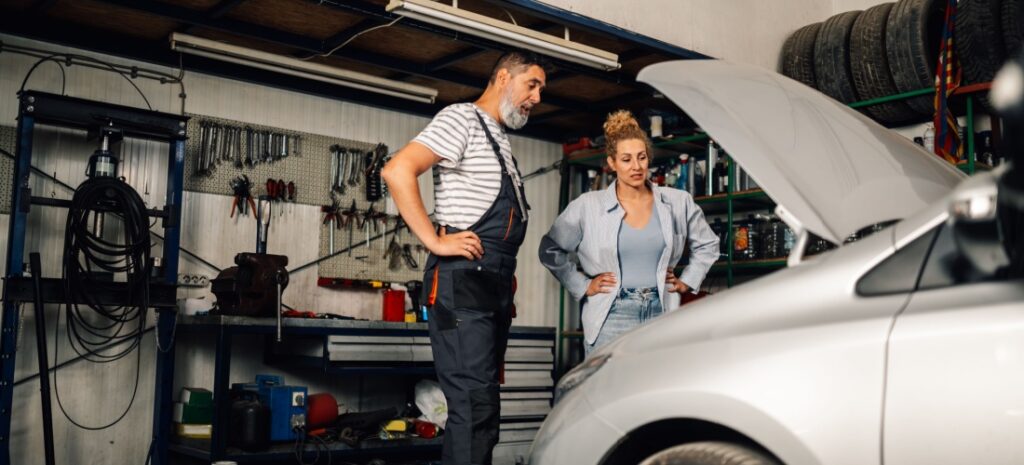 Mecánico observando el motor del coche de una clienta, ambos están serios ante la situación